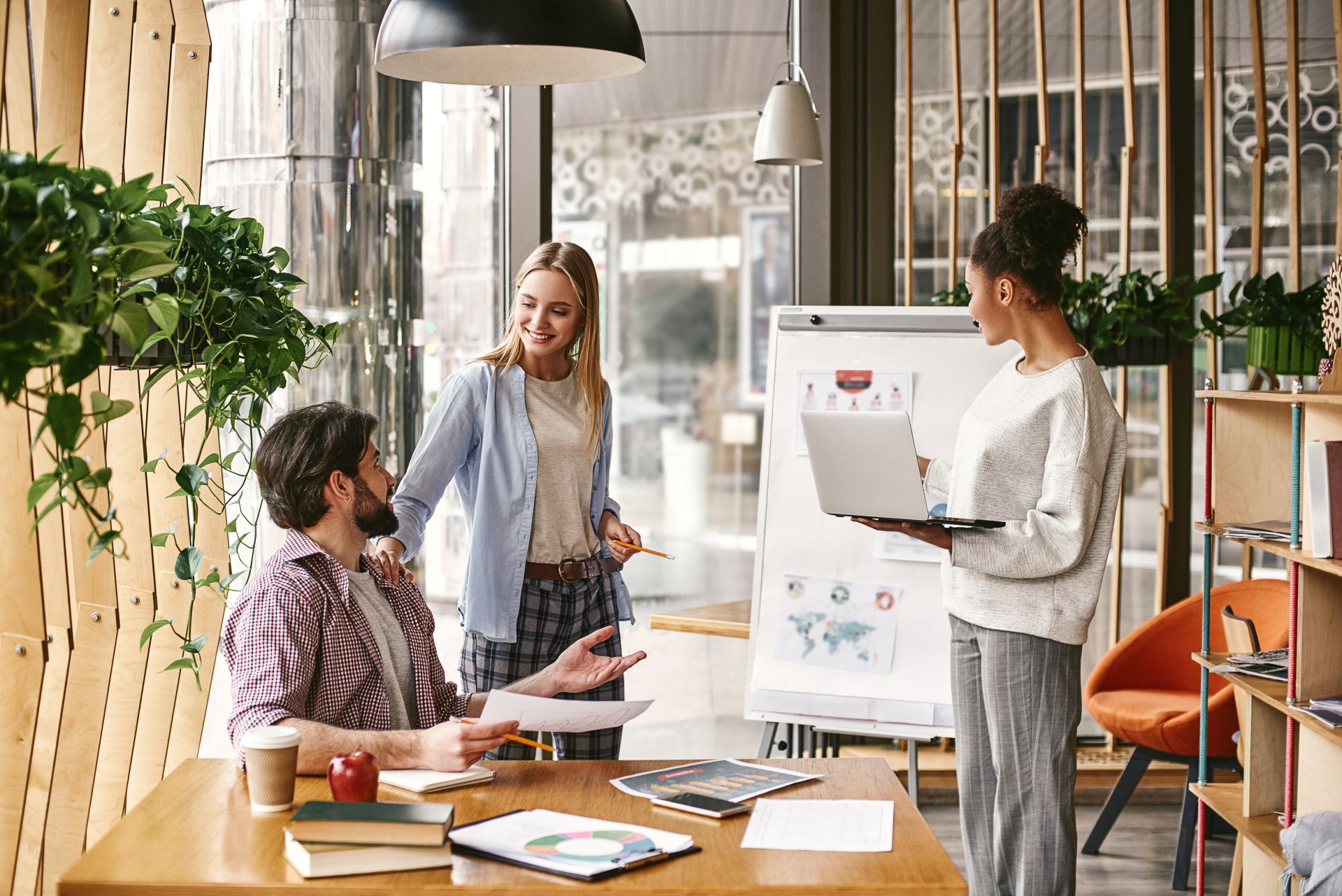 Team von Marketingfachleuten in einem modernen Büro diskutiert eine Strategie, während eine Frau mit einem Laptop vor einem Flipchart präsentiert