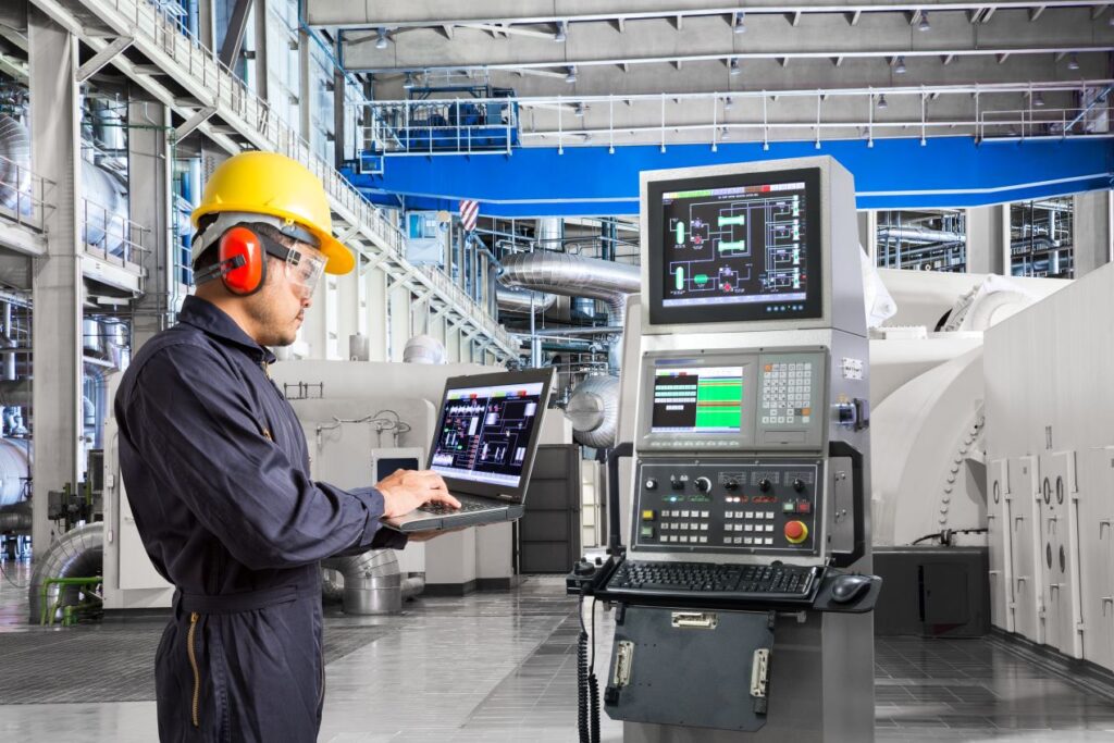 Technician in industrial facility using laptop and monitoring systems to check vacuum gauges and process control