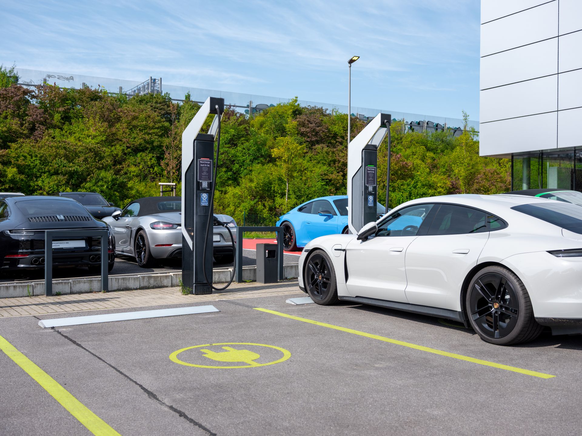 Elektrofahrzeuge auf markiertem Parkplatz mit E-Ladesäulen vor einem modernen Firmengebäude