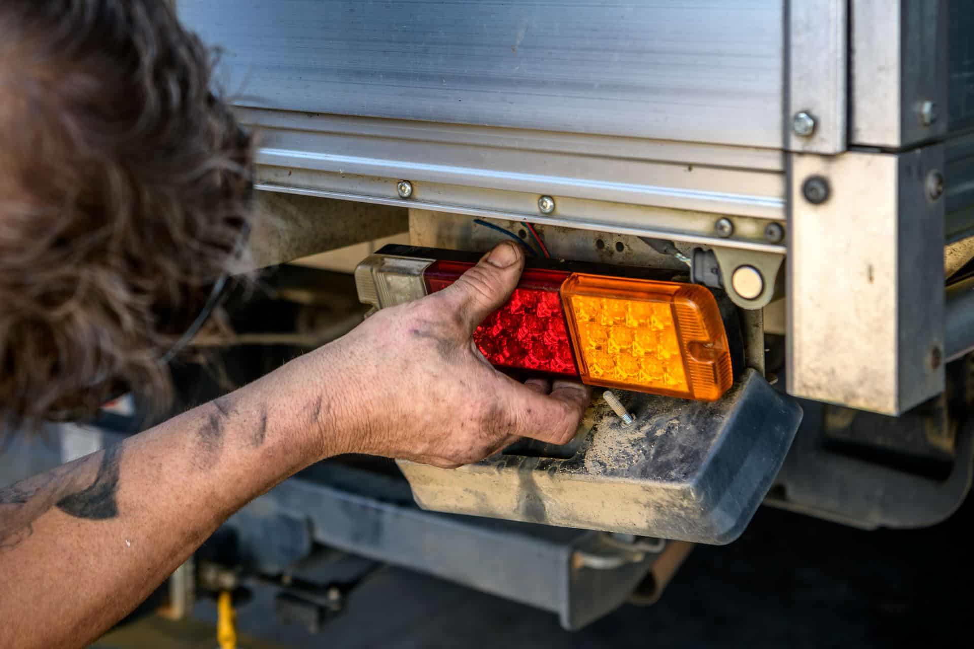 Mechaniker repariert Rückleuchte an einem LKW; verdeutlicht Wartung, Praxisnähe und die Wichtigkeit funktionierender LKW Beleuchtung.